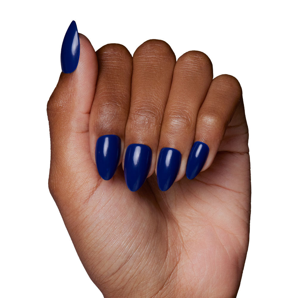 A hand with medium brown skin and long, almond-shaped nails wears the glossy Midnight Blue press-ons by glamnetic, crafted vegan & cruelty-free, displayed against a white background. - Product image