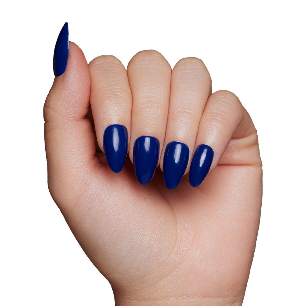 A hand with long, almond-shaped nails painted in the glossy, vegan, and cruelty-free Midnight Blue press-on nail set by glamnetic, shown against a plain white background. - Product image