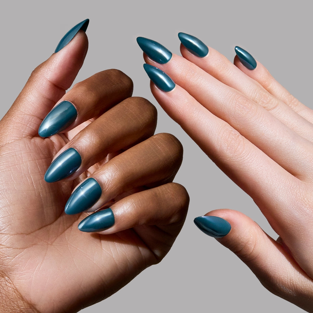 Two hands—one darker-skinned, one lighter—show off glamnetic's Midnight Teal press-on nails. Their almond shape and salon-quality finish pop against a plain gray background. - Product image