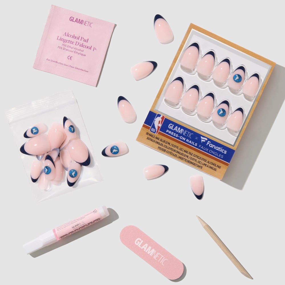 The glamnetic Minnesota Timberwolves Press-On Nail Set features pink nails with navy tips and a blue logo, displayed on a light surface with an alcohol pad, pink nail glue, nail file, cuticle stick, and extra nails. - Product image