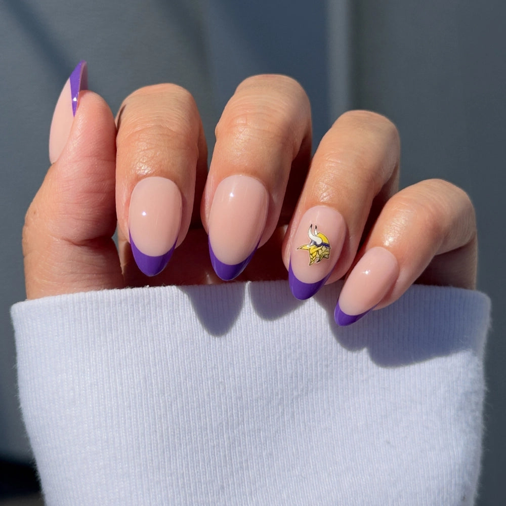 Show off your Minnesota Vikings pride with glamnetic’s Minnesota Vikings Press-On Nail Set—almond-shaped nails in light pink with purple French tips and a yellow Viking head accent. Perfect for any fan, styled here with a white long-sleeve top.