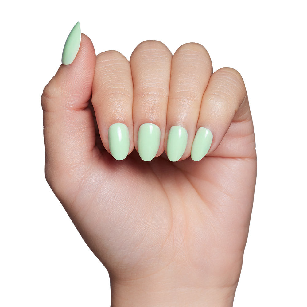 A hand with neatly manicured nails showcases the glamnetic Mint Green Nail Set in a short oval shape, each nail painted a glossy pastel mint green and displayed against a white background, fingers curled to highlight the shine. - Product image