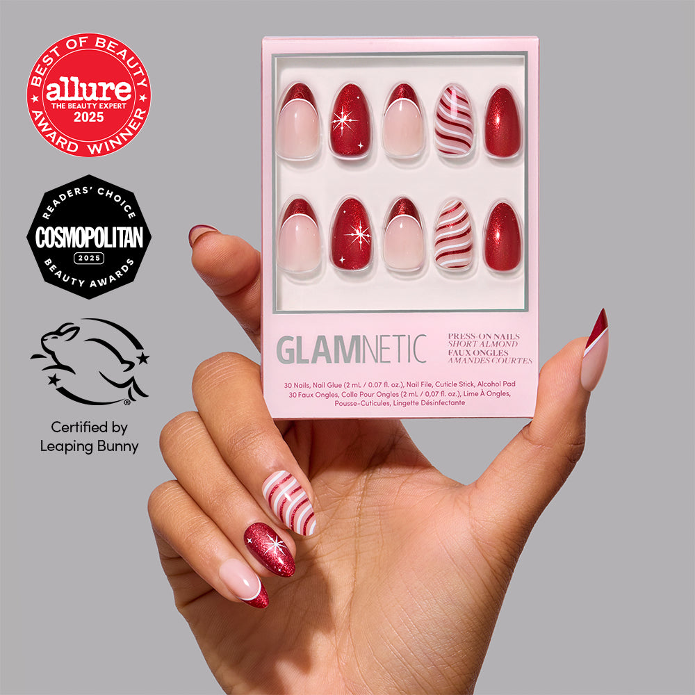 A hand holds a box of Glamnetic Mint to Be short almond-shaped press-on nails featuring red and white candy cane-inspired designs, glitter accents, and beauty award logos.