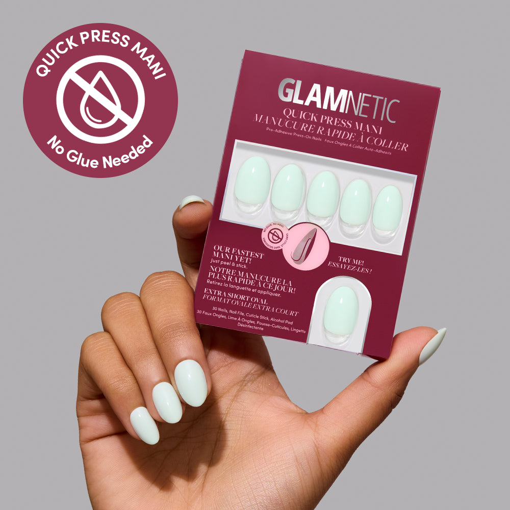 A hand holds a box of Minty Cloud extra short, oval, mint green press-on nails by Glamnetic next to a Quick Press Mani circular badge. - Product image