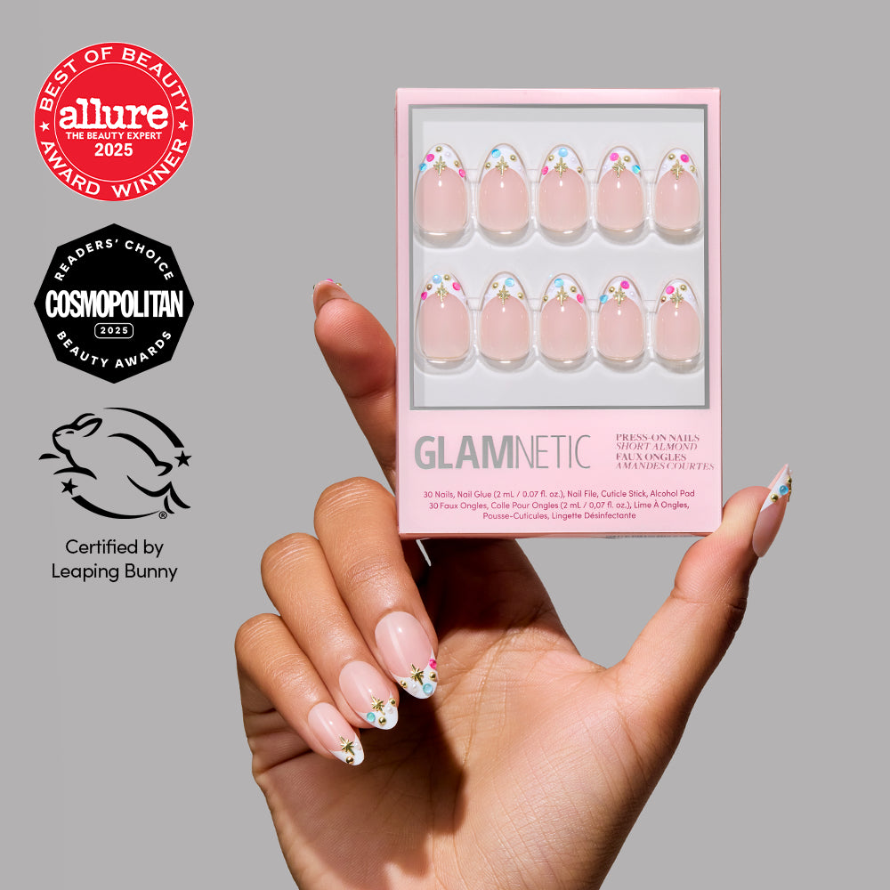 A hand with nude, almond-shaped nails featuring jewel accents holds the Moonstone press-on nail kit by glamnetic. The matching packaging is shown, along with beauty award logos and the Certified by Leaping Bunny logo.