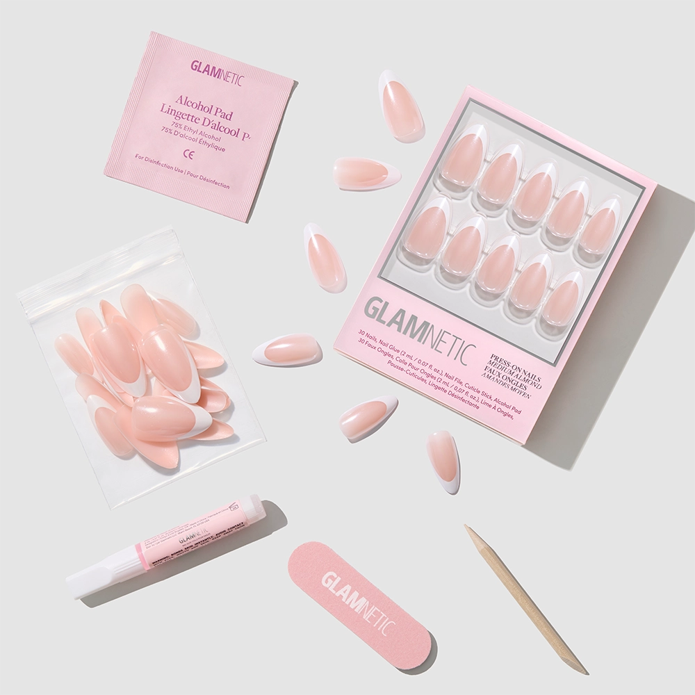 A flat lay of the glamnetic Mother Pearl Press-On Nails kit displays glossy pink nails, a wooden cuticle stick, nail file, alcohol pad, and glue arranged on a light gray background. - Product image