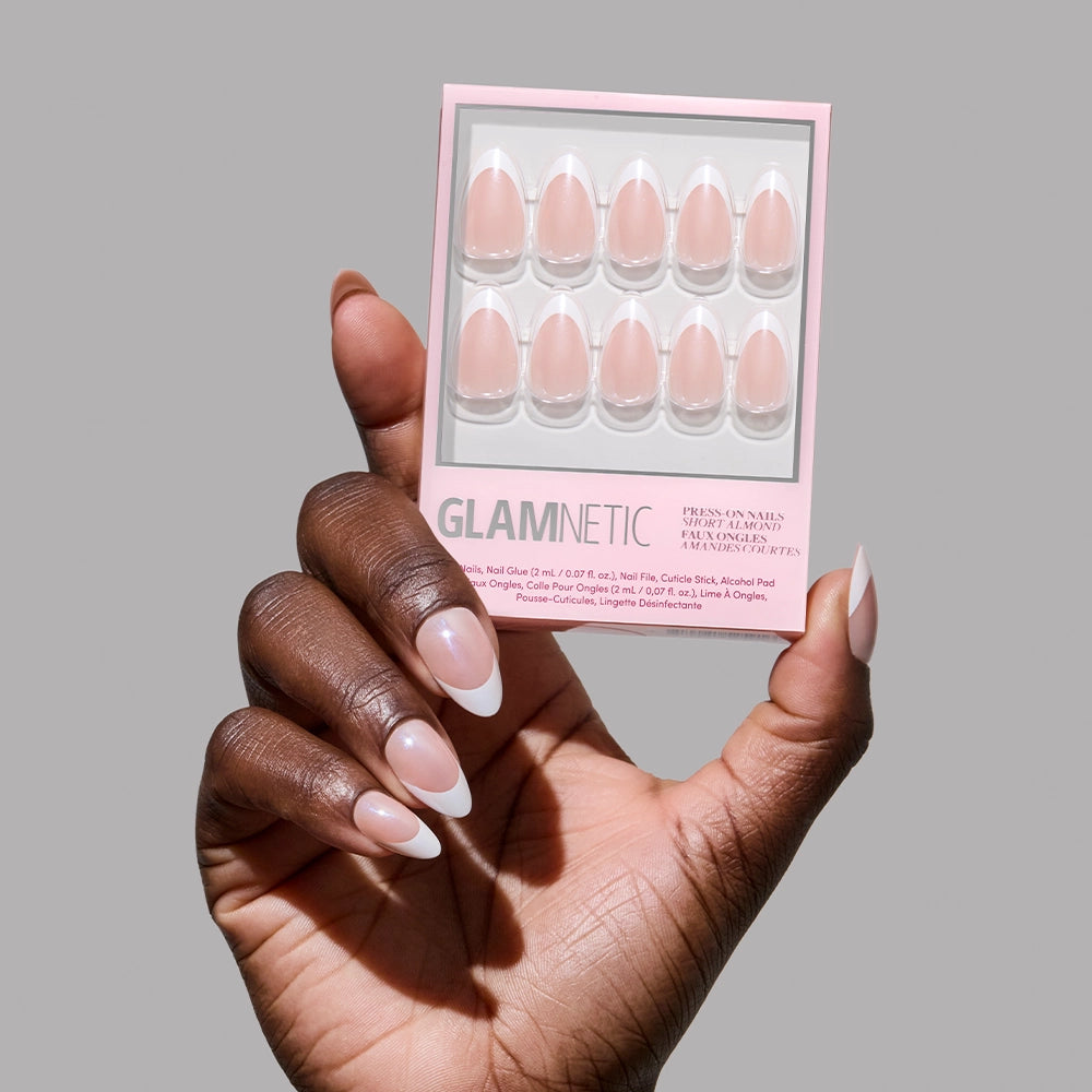 A hand with long, almond-shaped French tip nails holds a glamnetic "Mrs." press-on nail set featuring ten pink French-tip nails—an ideal chic bridal look—against a plain grey background. - Product image