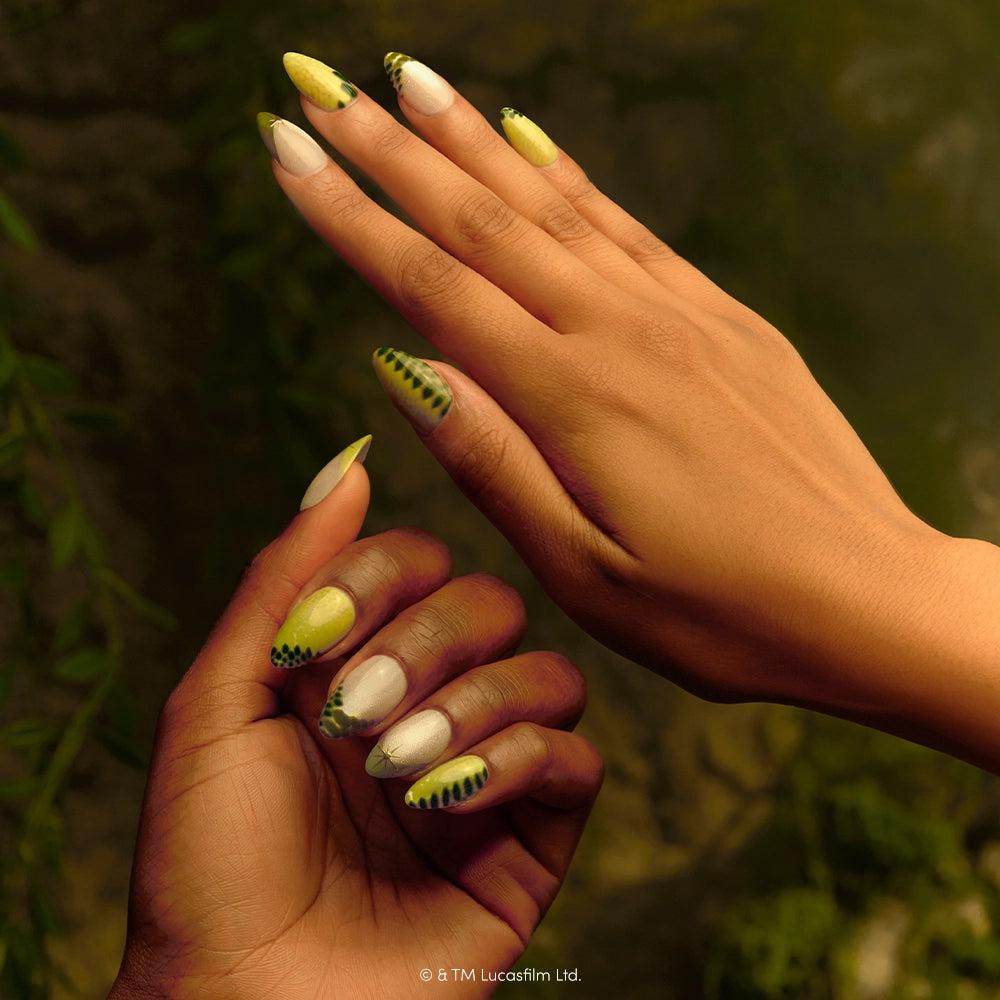 Much To Learn, You Still Have - Two hands with long, almond-shaped nails painted in green, white, and black patterns inspired by snake or reptile scales—a design reminiscent of the forest moon—feature the “Much To Learn, You Still Have” press-on nails by glamnetic, perfect for Star Wars fans seeking a unique manicure.