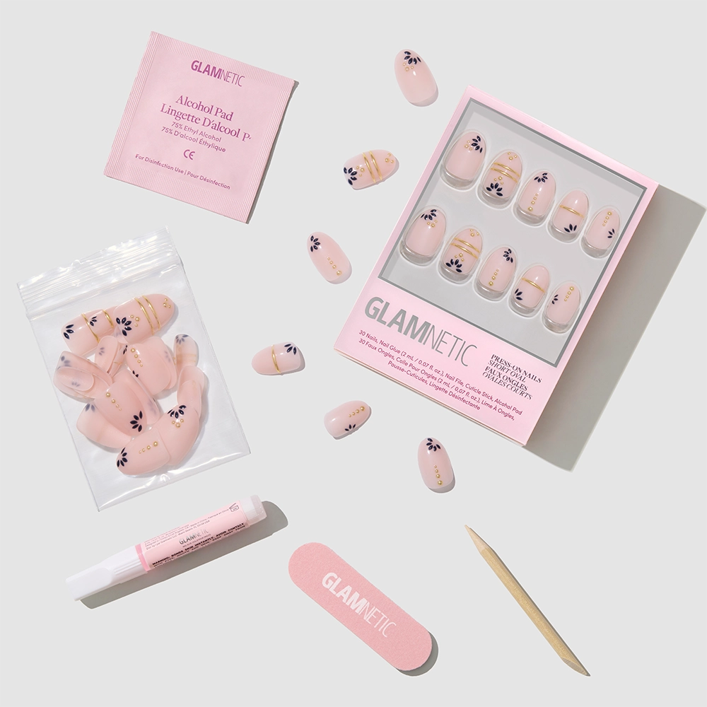 The Myko Muse press-on nails by glamnetic feature pink, short oval tips with black flower designs and come with a nail file, wooden cuticle stick, nail glue, alcohol pad, and extra nails arranged on a light background. - Product image
