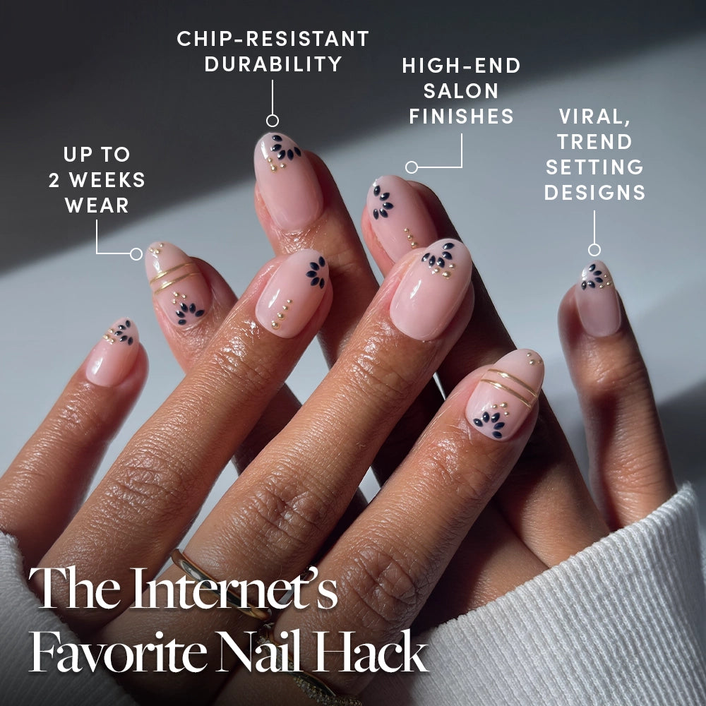 A close-up of hands with glossy, nude-pink short oval Myko Muse press-on nails from glamnetic, featuring gold lines and navy flower details—durable nails with long wear, a salon finish, and trendy Greek-inspired designs. - Product image