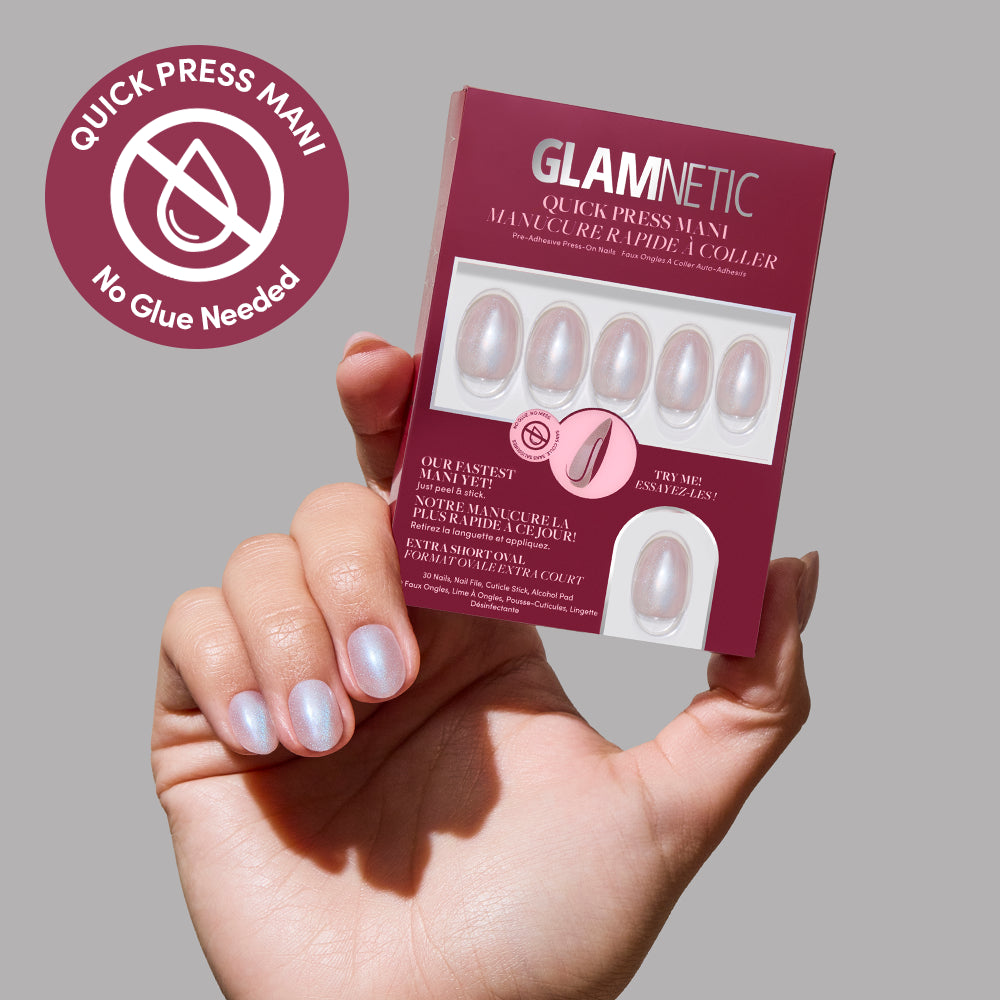 A hand with pearly, light pink press-on nails holds a burgundy glamnetic box labeled Nude Glazed. Six stick-on nails are displayed inside, and a round label reads, Quick Press Mani, No Glue Needed.