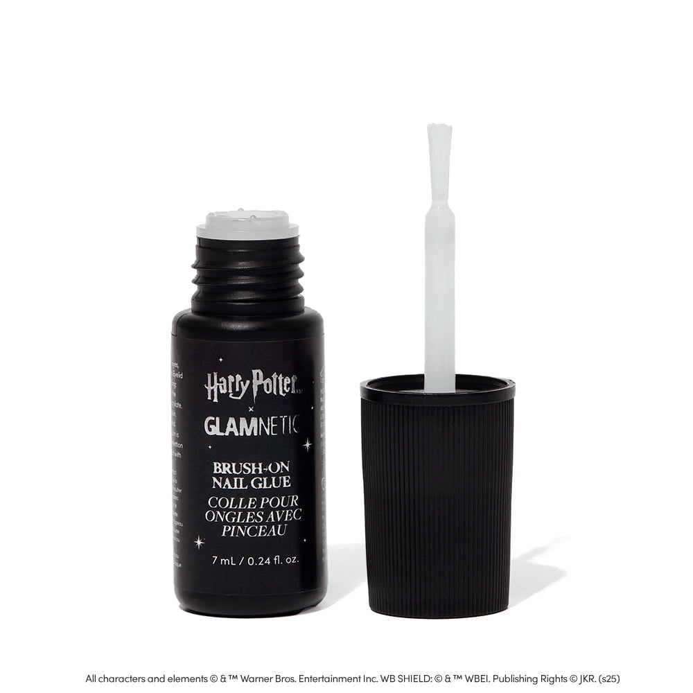 A black bottle of glamnetic Harry Potter™ x Glamnetic Brush-On Nail Glue stands upright with the cap off, showing its brush applicator—ideal for press-on nails. The label displays both English and French text.