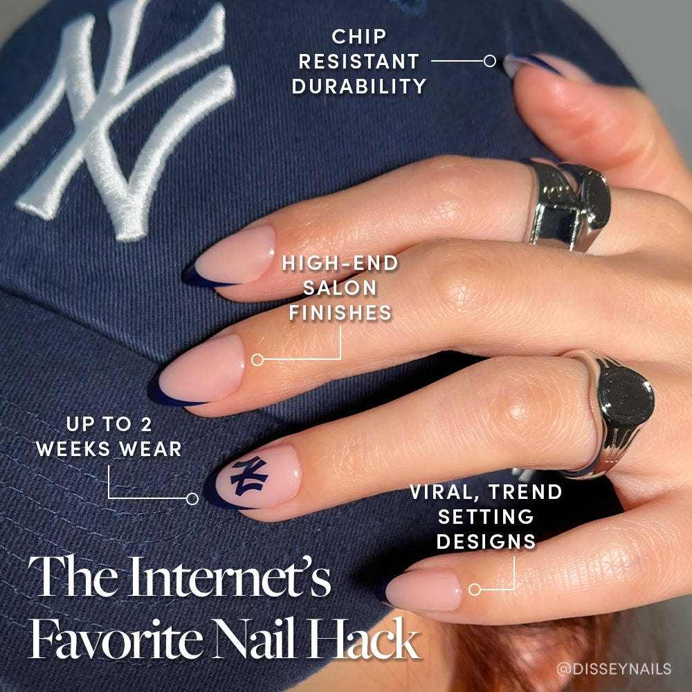 A hand with glossy nude glamnetic New York Yankees Press-On Nails, one featuring the Yankees logo, rests on a Yankees cap. Chip-resistant, salon-quality finish, trendy designs, and up to 2 weeks’ wear are highlighted. - Product image