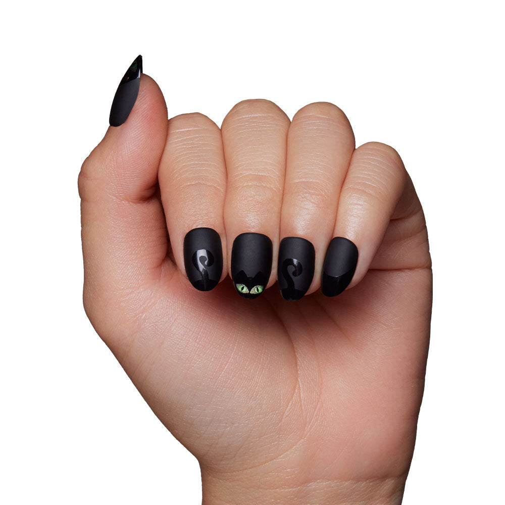 A hand with glamnetic’s Nine Lives matte black cat nails, showing a velvet-finish cat eye design on the middle finger and small green cat eyes on the ring finger, against a white background. - Product image