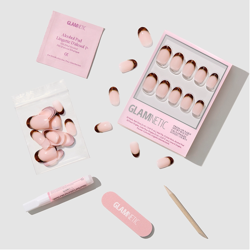 The No Apologies press-on nail set by glamnetic features pink and rose gold short round nails, glue, alcohol pad, nail file, cuticle stick, and extra nails arranged neatly on a white background with the glamnetic logo visible. - Product image