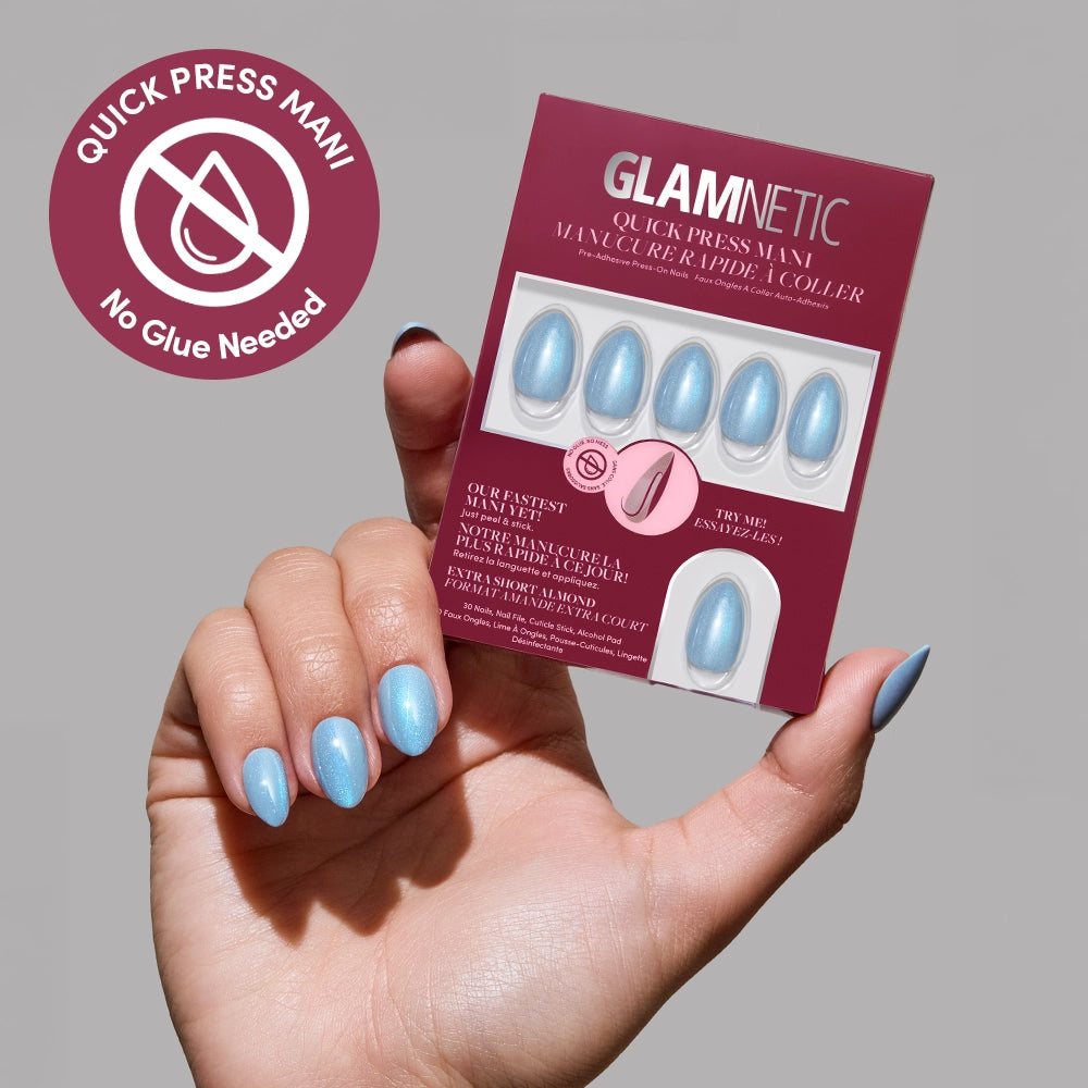 A hand with light blue, almond-shaped press-on nails holds a glamnetic Ocean Prism Quick Press Mani box, which displays matching no-glue nails and a “No Glue Needed” symbol in the corner.