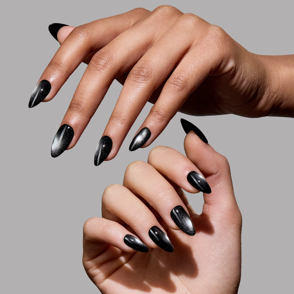 Two hands with glamnetic Obsidian press-on nails, long almond-shaped and glossy black with a metallic sheen, are posed elegantly against a plain gray background.