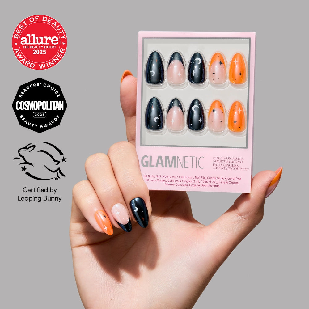 A hand displays orange and black “October Nights” press-on nails with star designs, holding a box of glamnetic nails. Beauty award logos and a cruelty-free certification appear to the left on a gray background, highlighting these short almond nails as both stylish and convenient. - Product image