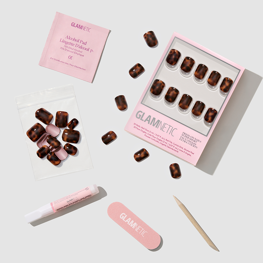 The glamnetic Own It All set features medium oval tortoiseshell French tip press-on nails, nail glue, a pink file, cuticle stick, alcohol pad, and a resealable bag—neatly arranged on a light background. - Product image