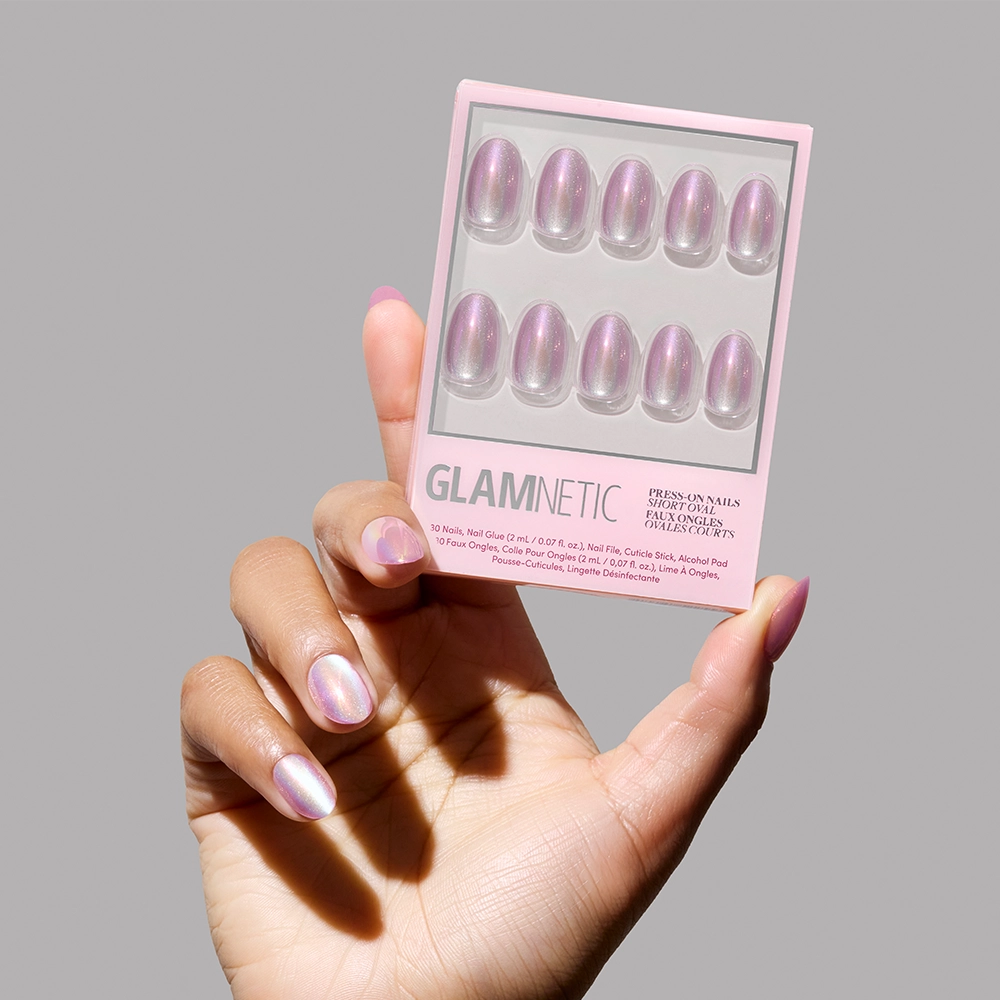A hand with iridescent pink press-on nails holds glamnetic’s Oyster set, which includes ten pearlescent purple nails in assorted sizes, shown against a simple background. - Product image