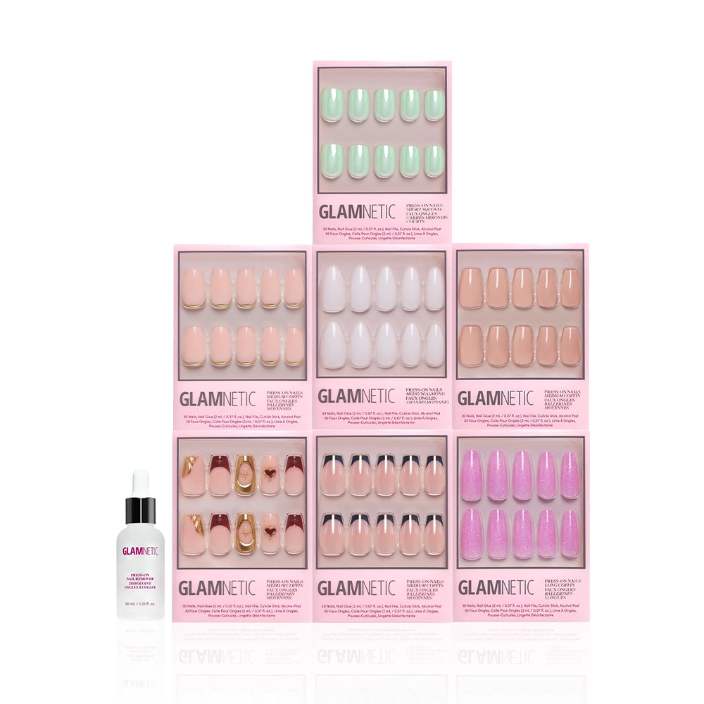 Seven boxes of glamnetic Main Stage Moment press-on nails in various colors and designs are stacked in a pyramid shape, with a bottle of glamnetic nail glue positioned in front on a white background. - Product image