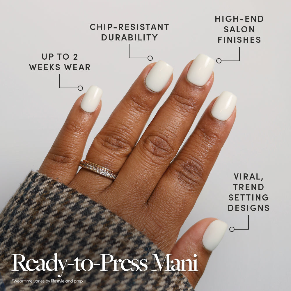A hand with Porcelain, glossy white no-glue press-on nails by glamnetic is shown, featuring up to 2 weeks wear, chip-resistant durability, salon-quality finishes, and trend-setting designs. The hand wears a ring and a plaid sleeve. - Product image