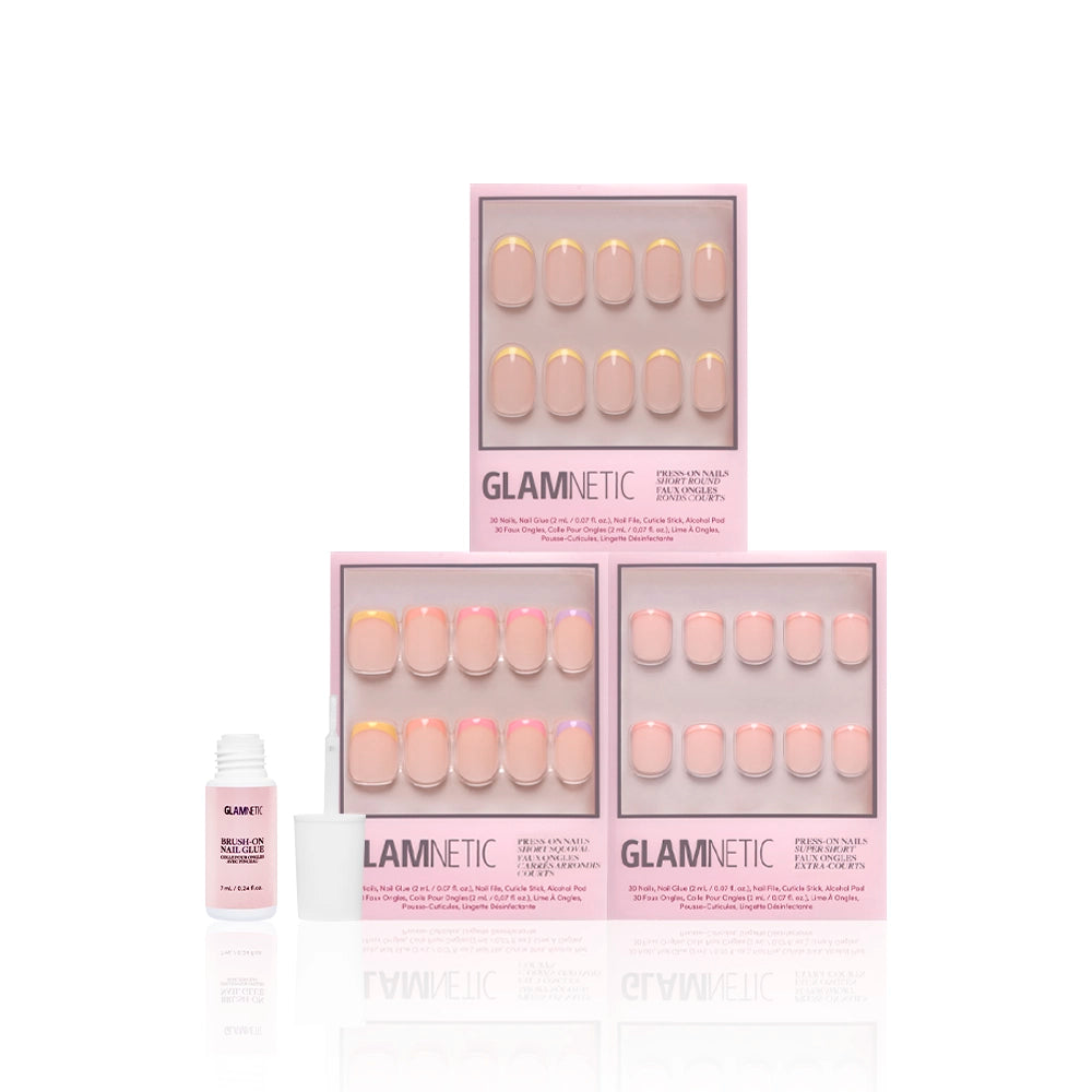 Three boxes of glamnetic’s Pardon My Pastels press-on nails are stacked in a pyramid, featuring pastel pink and yellow French tips. A small white bottle of nail glue with its cap off is placed to the left of the boxes. - Product image