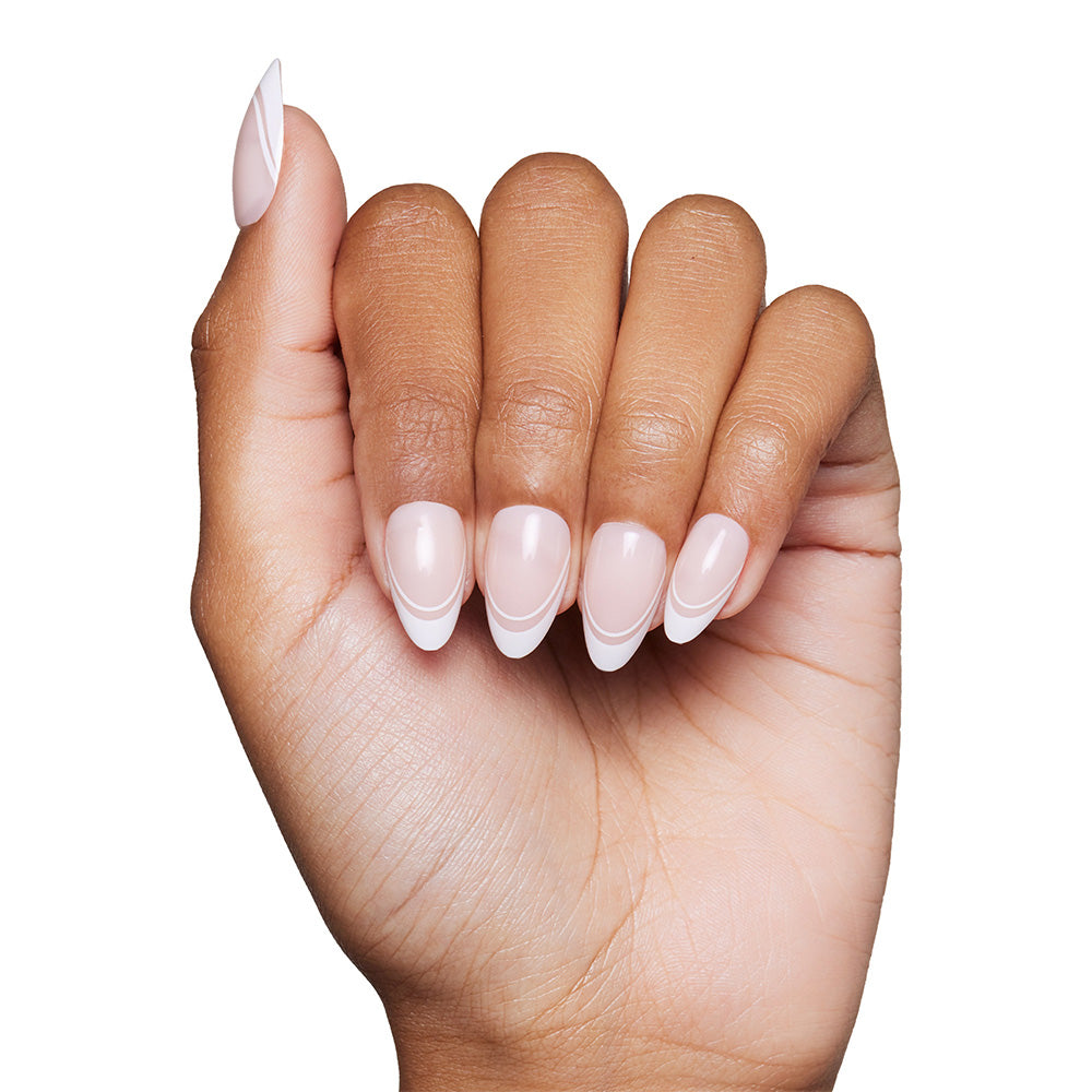 A hand with medium brown skin displays short almond nails styled in a classic French manicure, created using glamnetic’s Paris press-ons—pale pink base and white tips—set against a plain white background for timeless elegance. - Product image