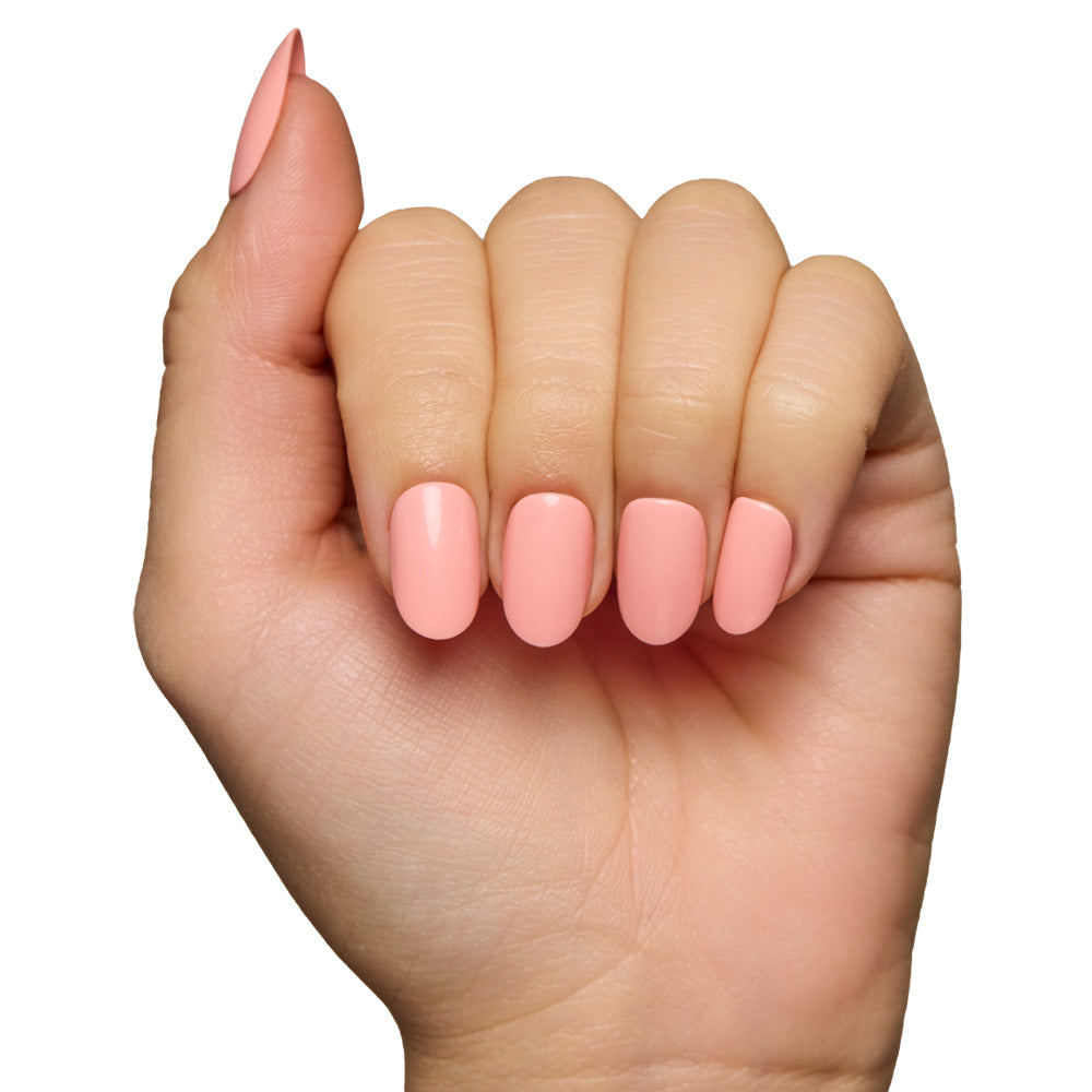 A hand with fingers slightly curled showcases glamnetic’s reusable Peach Coral nails, painted in a glossy pastel peach shade, against a white background. - Product image
