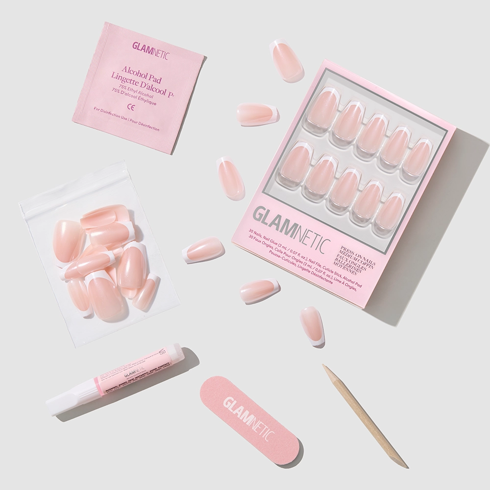 A flat lay shows the glamnetic Pearl Glaze Press-On Nails kit with medium coffin pink nails, extra nails, an alcohol pad, glue, pink file, and a wooden cuticle stick on a light grey background. - Product image
