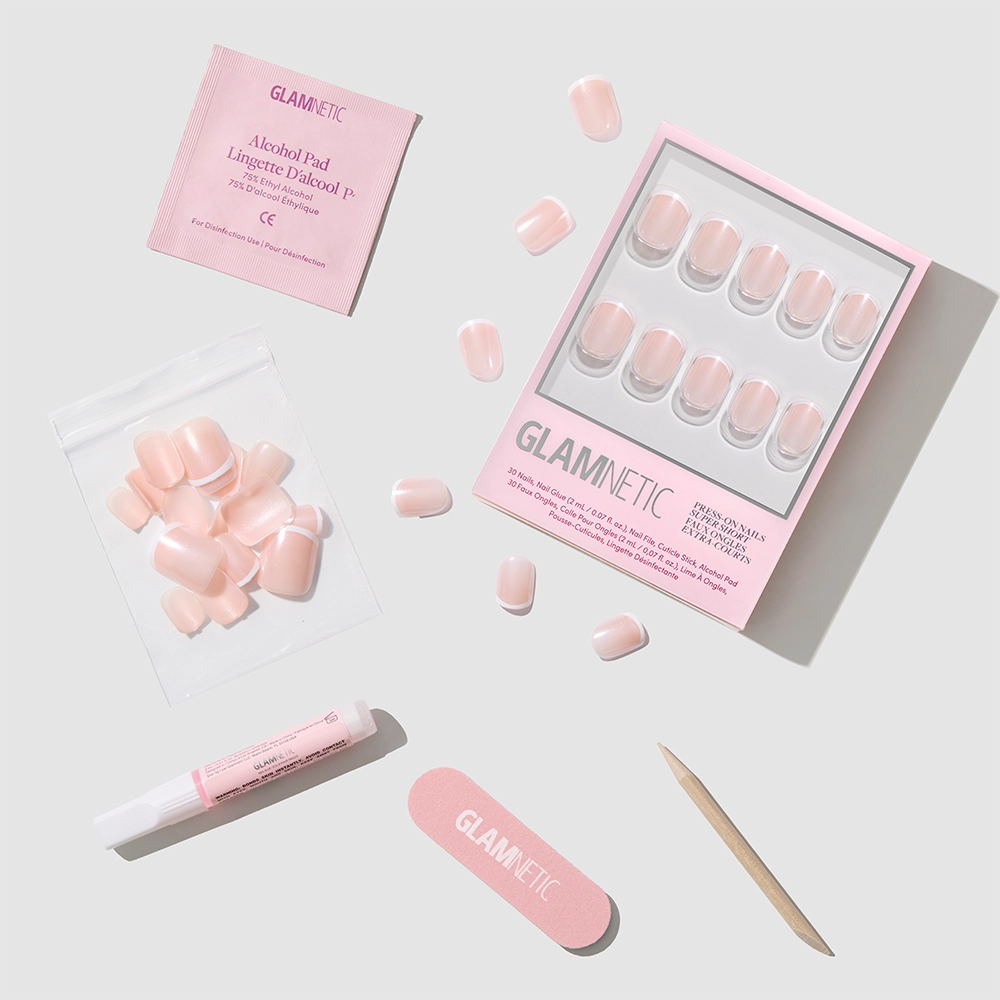 The Pearly Please Press-On Nails by glamnetic, featuring a glossy glazed finish, come with a pink nail file, wooden cuticle stick, alcohol pad, nail glue, and extra nails, all neatly arranged on a light gray background. - Product image