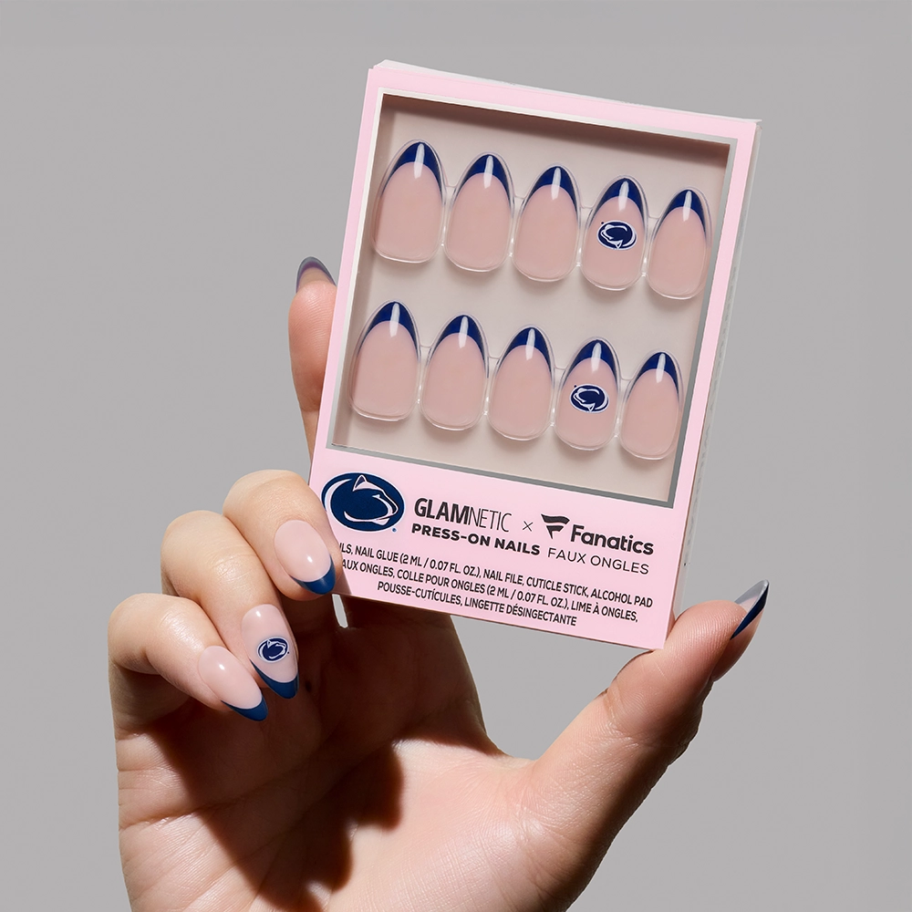 A hand holds the glamnetic Penn State Nittany Lions Press-On Nail Set, featuring officially licensed nude nails with dark blue French tips and some with the team’s lion head logo.