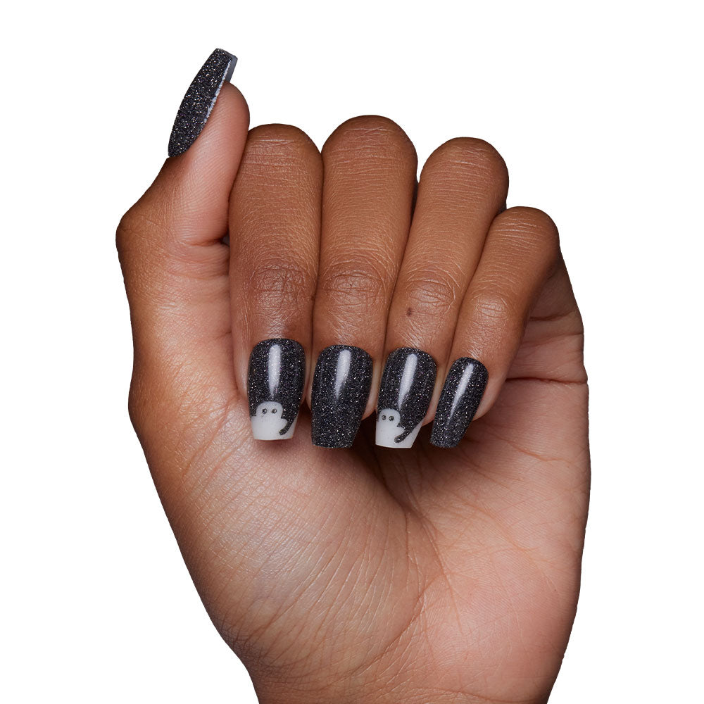 A hand features long, coffin-shaped nails in glamnetic’s “Phantom Glow” style—black with a glittery finish. Two nails are accented with small white ghost designs. The background is plain white. - Product image