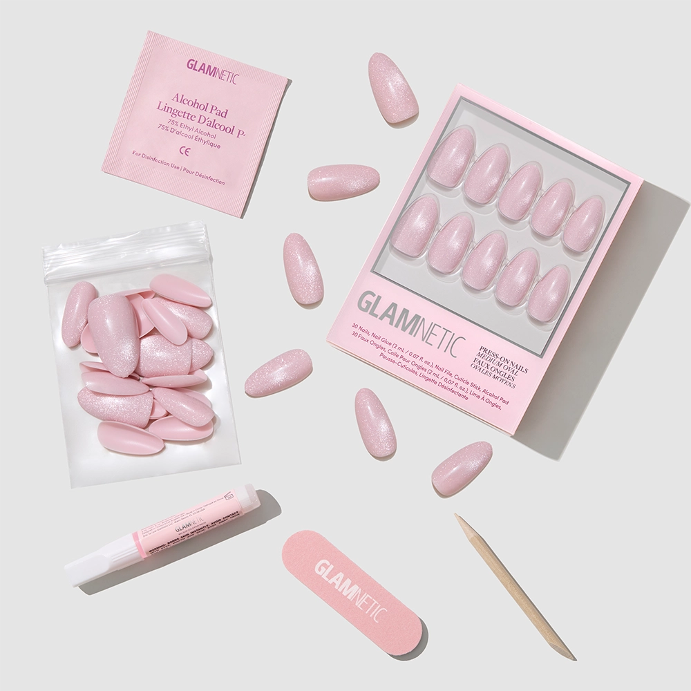 The glamnetic Pink Darling set includes salon-quality pink press-on nails, nail glue, a file, cuticle stick, alcohol pad, and extra nails—all in a matching pale pink shade—displayed on a light gray background.