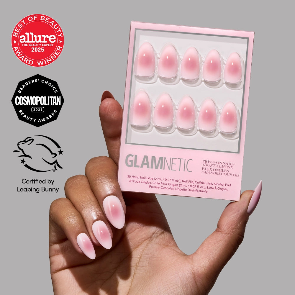 A hand with short almond Pink Petalite press-on nails by glamnetic holds a matching box. Allure, Cosmopolitan, and Leaping Bunny award badges are shown on the left against a light gray background. - Product image