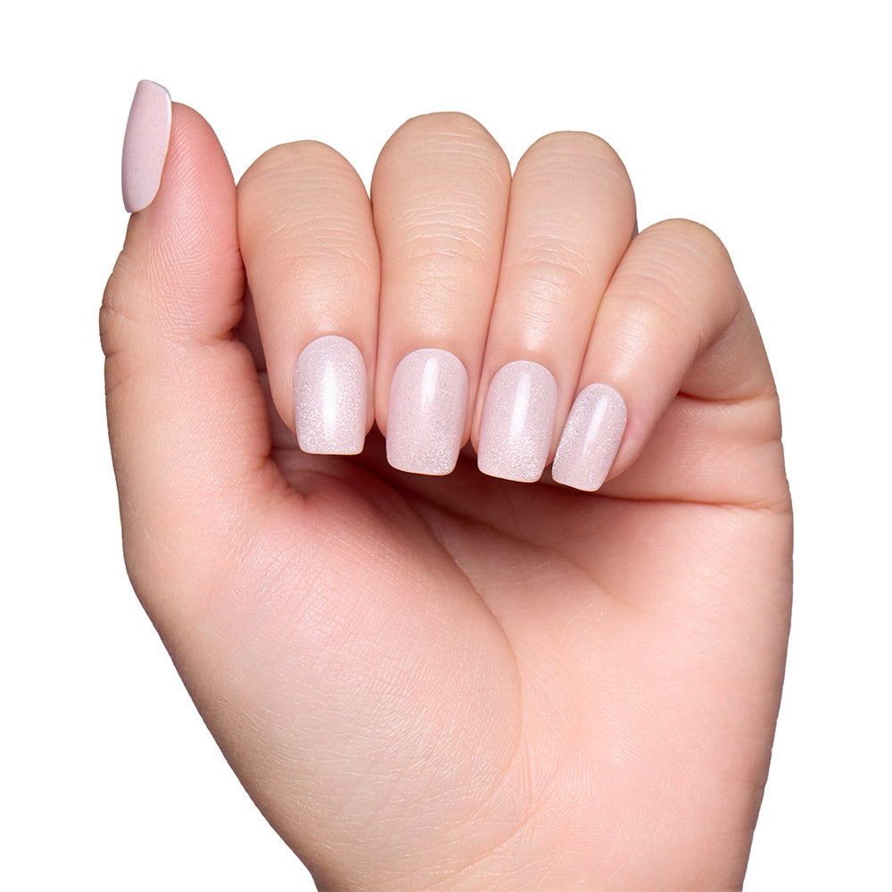A hand with short squoval nails is painted in glamnetics Pinky Promise—a pale, shimmery pink polish with a blush velvet finish—shown against a white background. - Product image