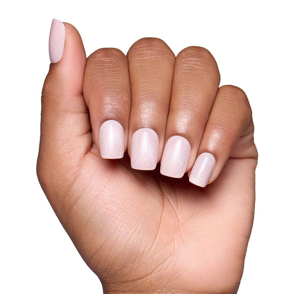 A hand with medium-brown skin displays short, squoval nails painted in glamnetic’s Pinky Promise—a light, shimmery blush pink—against a white background. - Product image