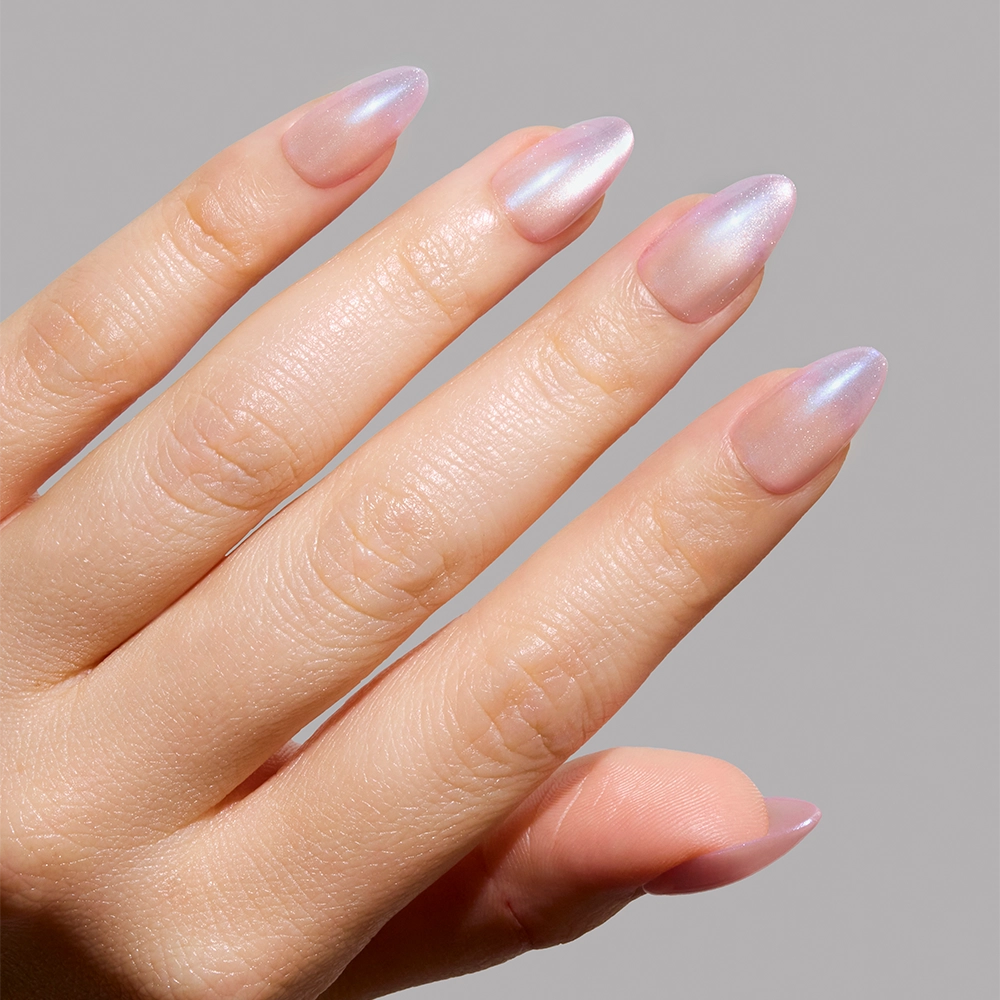 A hand with short almond nails showcases glamnetics Polar Day—a shiny, iridescent light pink and lavender manicure—reminiscent of velvet lilac nails, against a plain gray background. - Product image