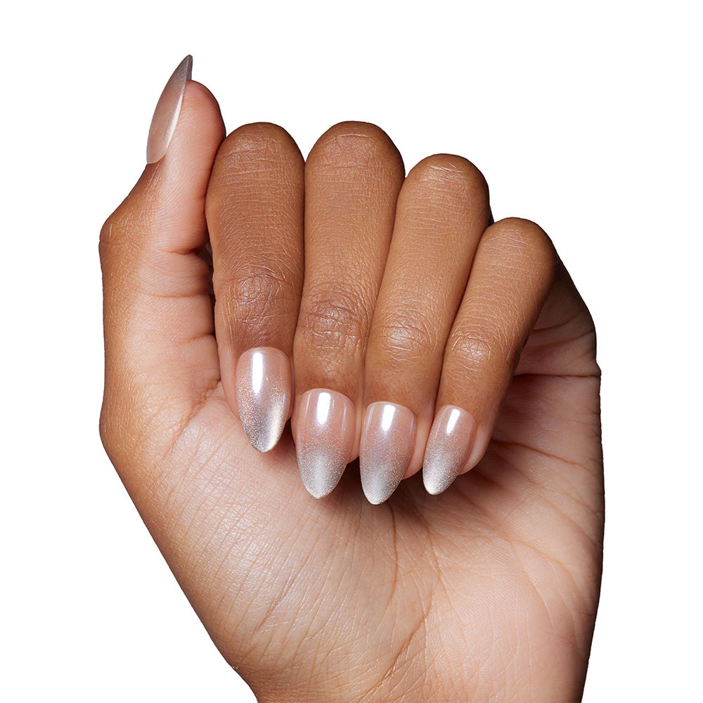 A hand with medium brown skin tone shows long, almond nails painted with glamnetic’s Polar Night—a shimmery, light pink polish with a glossy velvet finish—against a white background. - Product image
