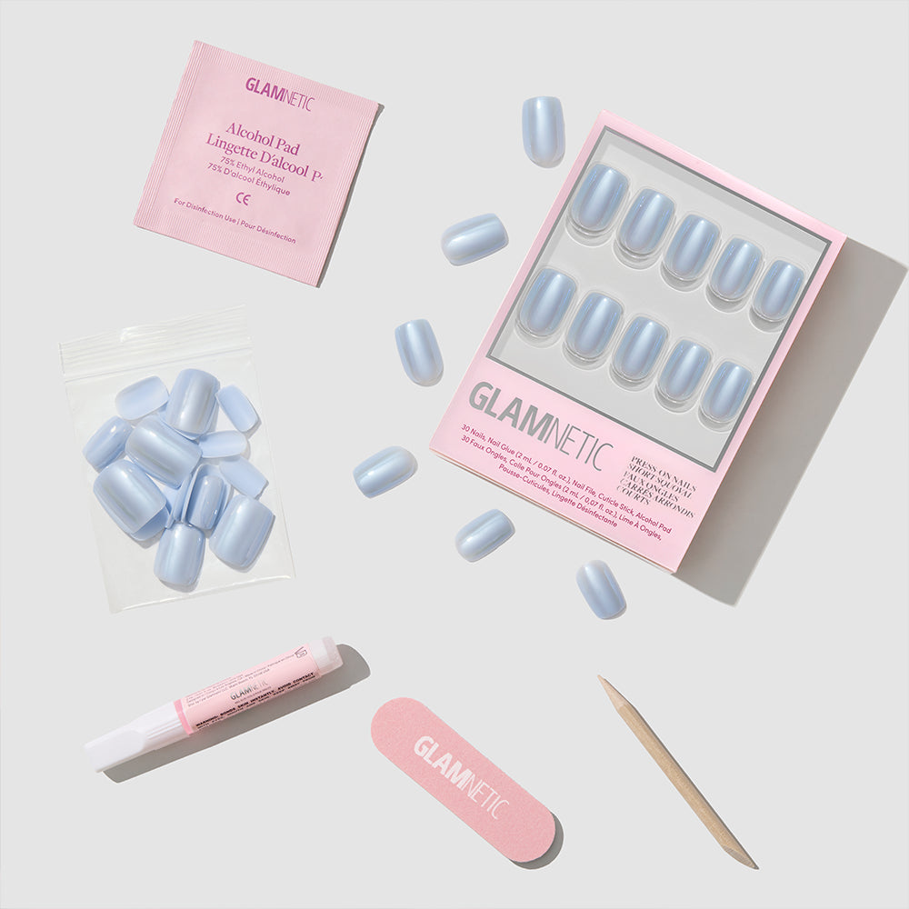 A glamnetic Powder Bleu kit featuring short, squoval press-on nails with a glazed finish, along with a nail file, glue, wooden cuticle stick, alcohol pad, and extra nails—all arranged on a light gray background. - Product image