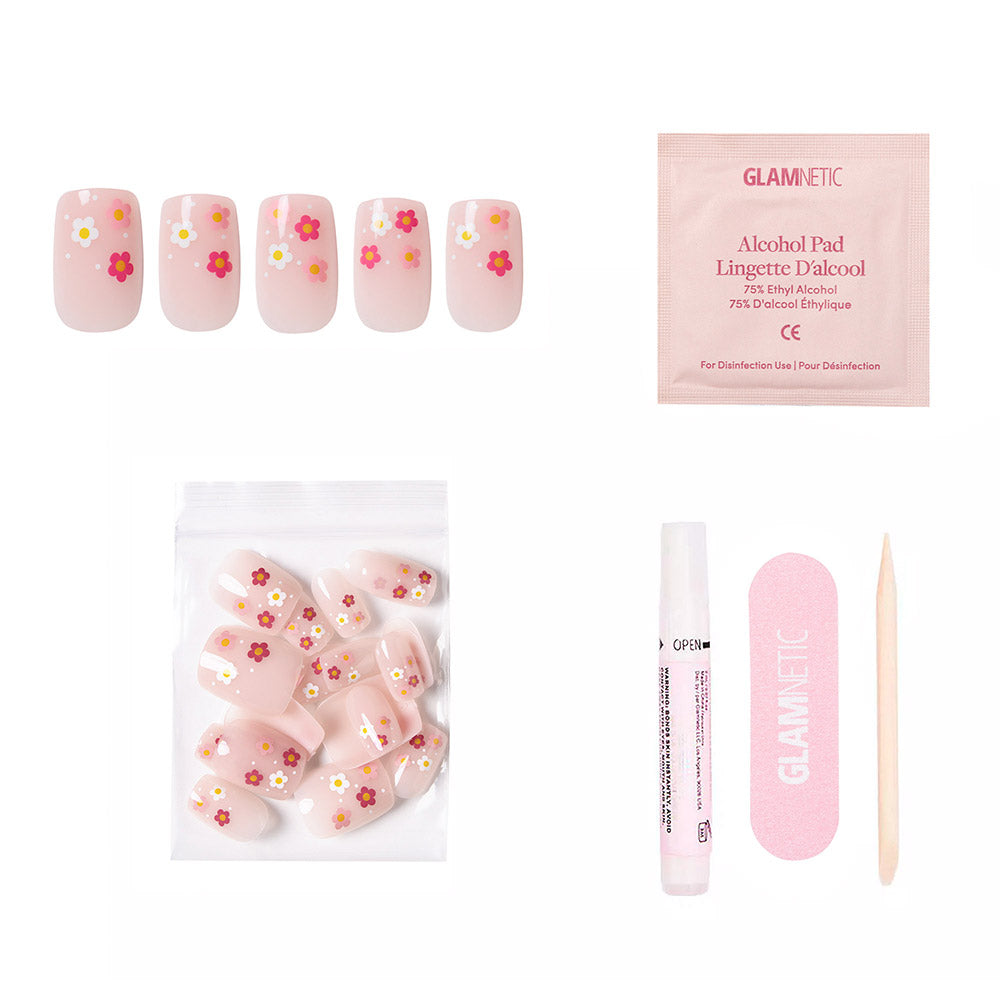 The glamnetic Pretty Bloom press-on nail kit features short, glossy pink squoval nails with red, yellow, and white floral French tips. Includes an alcohol pad, adhesive, cuticle stick, and a bag of extra nails. - Product image