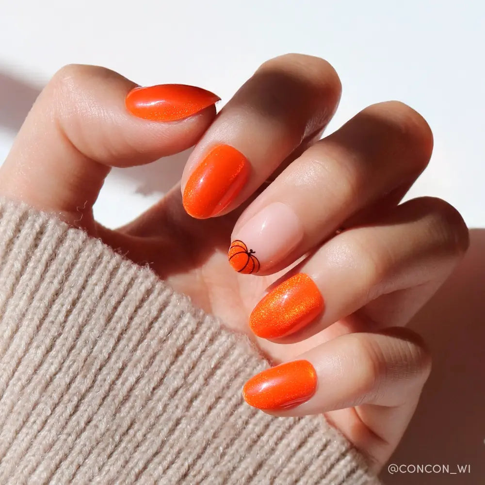 A hand wears glamnetic’s Pumpkin Patch set: glossy pumpkin orange velvet nails on four fingers, with a basketball design on the nude ring finger. The person is dressed in a beige knit sweater. - Product image