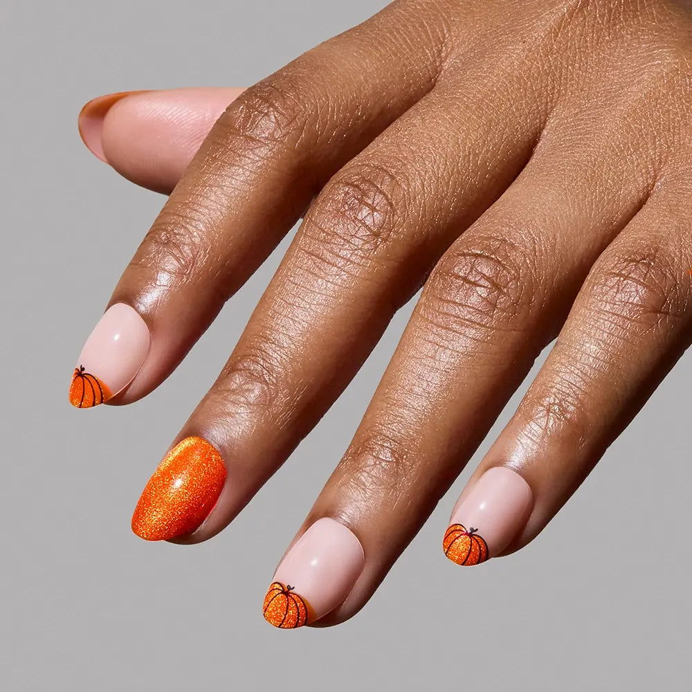 A hand displays the glamnetic Pumpkin Patch nails: manicured nails with basketball designs on three, a glittery pumpkin orange velvet accent, and a light nude base. This standout fall set pops against a plain gray background. - Product image