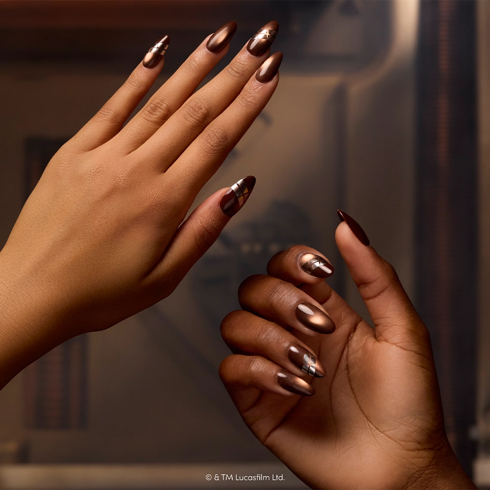 Two hands with long, almond-shaped nails decorated in shiny copper and metallic designs inspired by the glamnetic “Punch It, Chewie” set, held against a blurred brownish background. © & TM Lucasfilm Ltd. - Product image