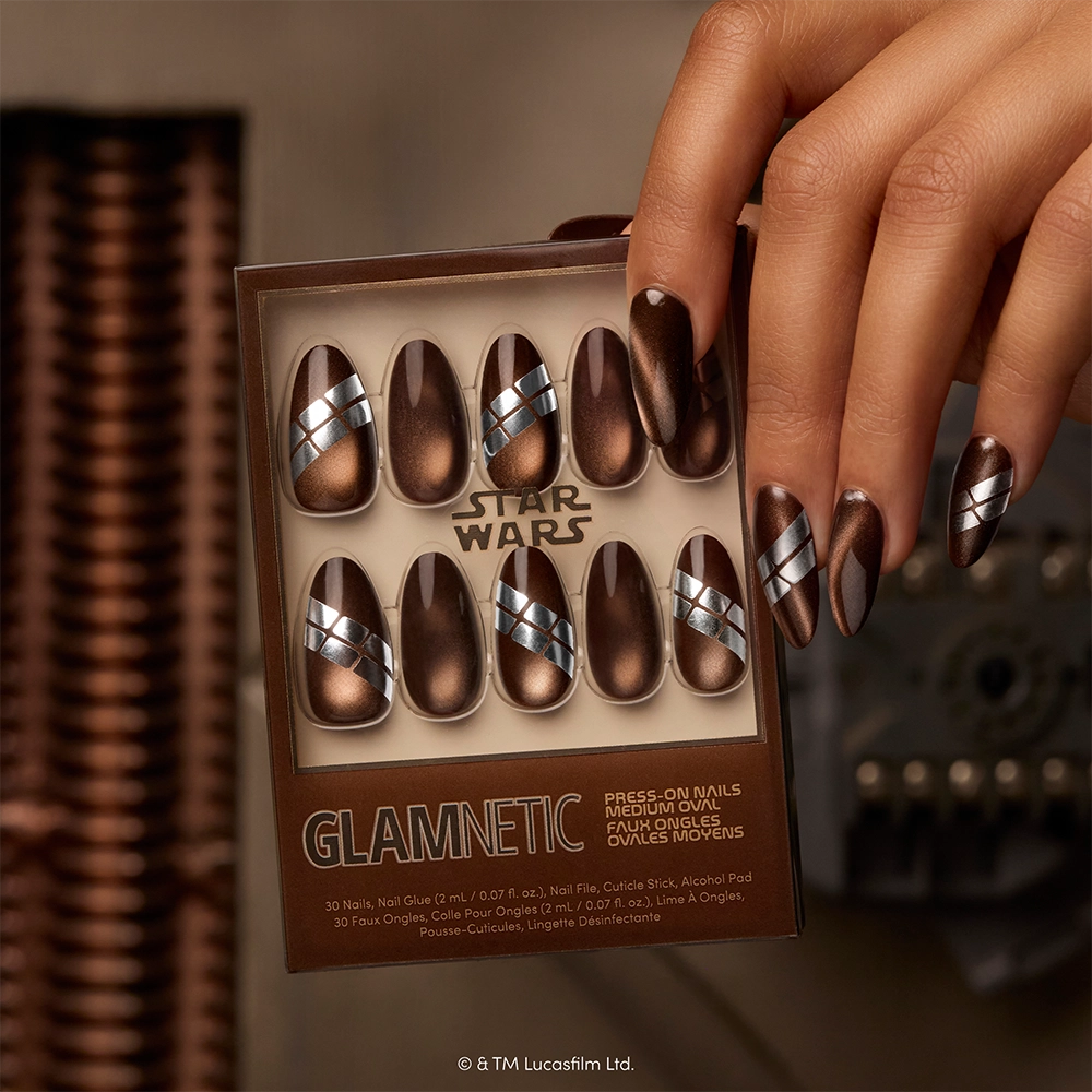 A hand displays the “Punch It, Chewie” metallic brown press-on nails with silver and blue stripes by glamnetic, while holding a Star Wars-themed Glamnetic nail set featuring similar designs. These vegan, cruelty-free nails are part of the limited-edition “Punch It, Chewie” collection—perfect for fans looking for bold Star Wars press-ons. - Product image