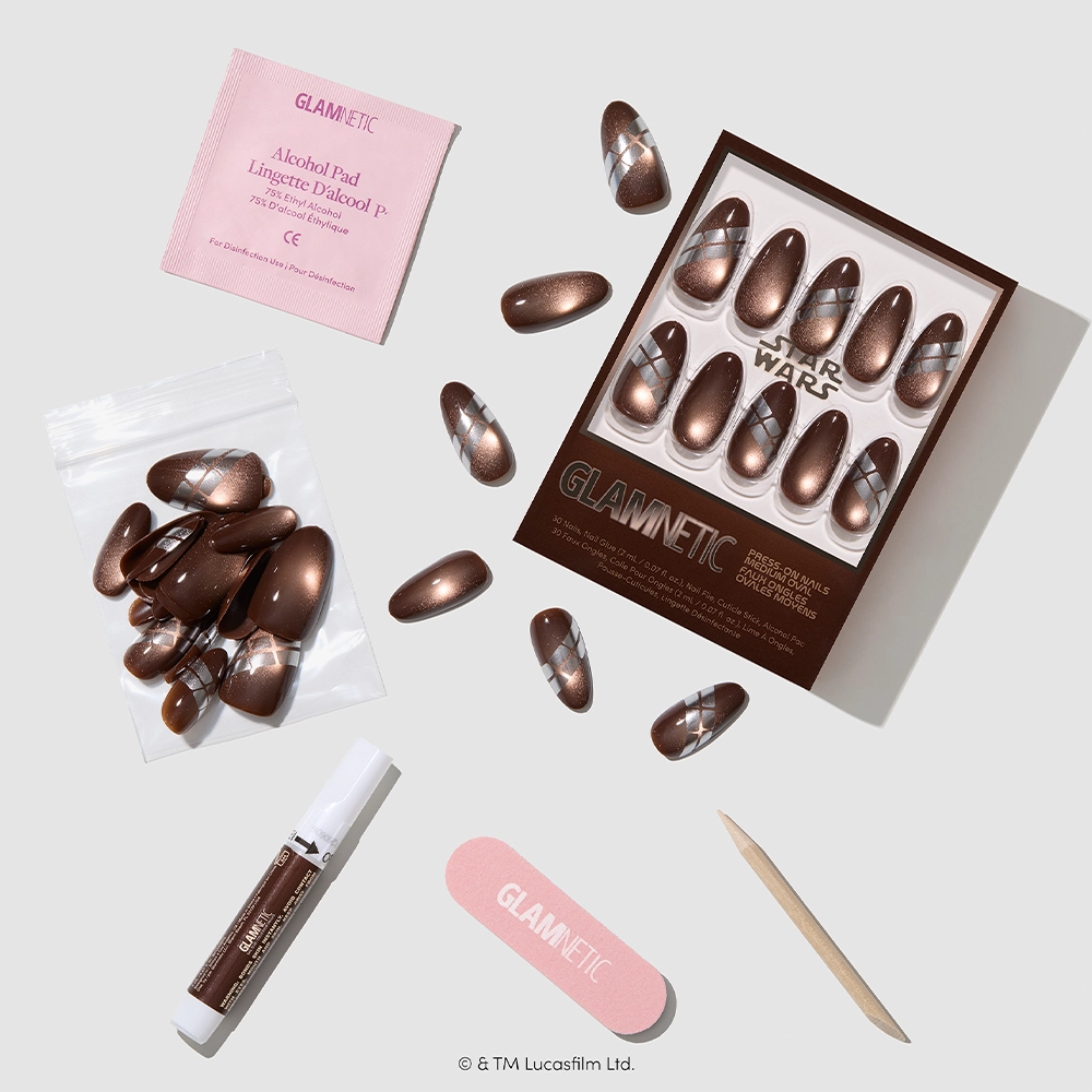Introducing “Punch It, Chewie” by glamnetic: a set of metallic brown Star Wars–inspired press-on nails celebrating Chewbacca. The set arrives with nail glue, an alcohol pad, nail file, wooden stick, and extra nails—all artfully presented on a white background. These vegan, cruelty-free nails come in packaging emblazoned with iconic Star Wars and glamnetic branding. - Product image