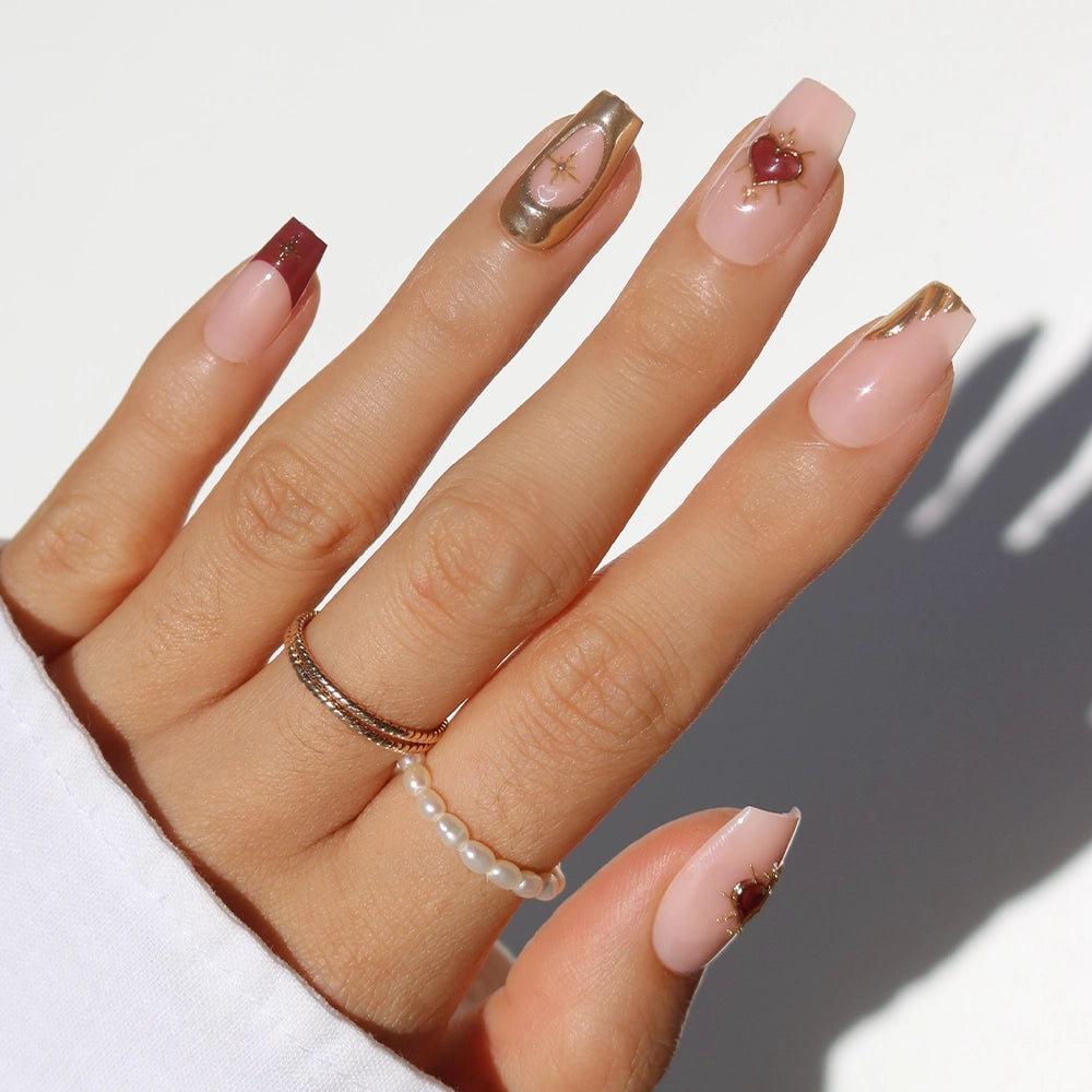 The "Queen of Hearts" nails by glamnetic feature medium-length, square-shaped coffin tips in nude, burgundy, and gold with gems and accents. Styled with gold and pearl rings, they’re perfect for chic 3D nail design lovers. - Product image
