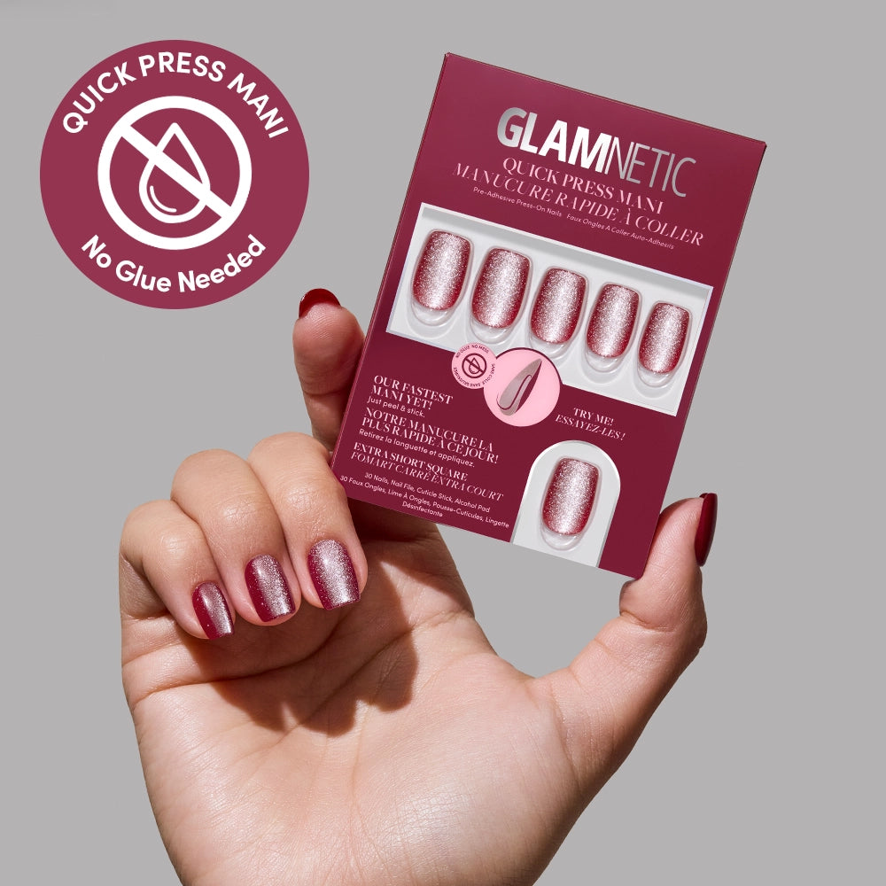 A hand with glittery pink no-glue nails holds a box of glamnetic Red Allure Quick Press Mani nails. The box shows matching nails, brand name, and a circular label highlighting Quick Press Mani and No Glue Needed.