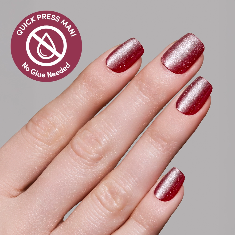 A hand with short, square-shaped nails features glamnetic’s Red Allure shimmery red press-ons. A circular label reads “QUICK PRESS MANI, No Glue Needed” with a crossed-out glue bottle, emphasizing these no-glue nails. - Product image