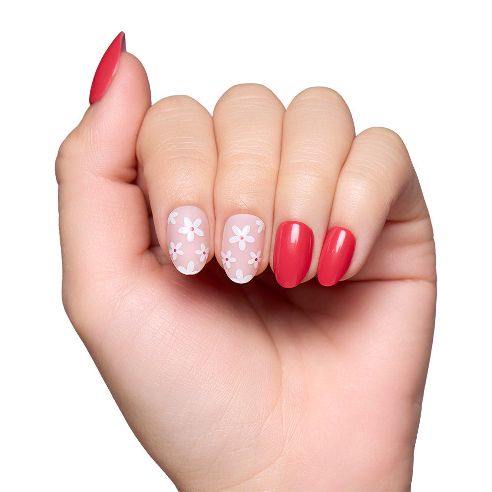 A hand models glamnetics Red Blossom nails: three solid coral pinks and two floral accents with pale pink bases and white daisies, all set against a white background. - Product image